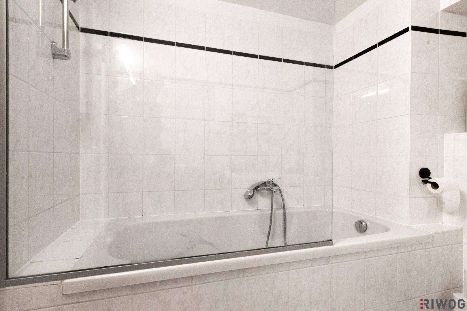 Saubere Badewanne mit Duschabtrennung in einem gefliesten Badezimmer.