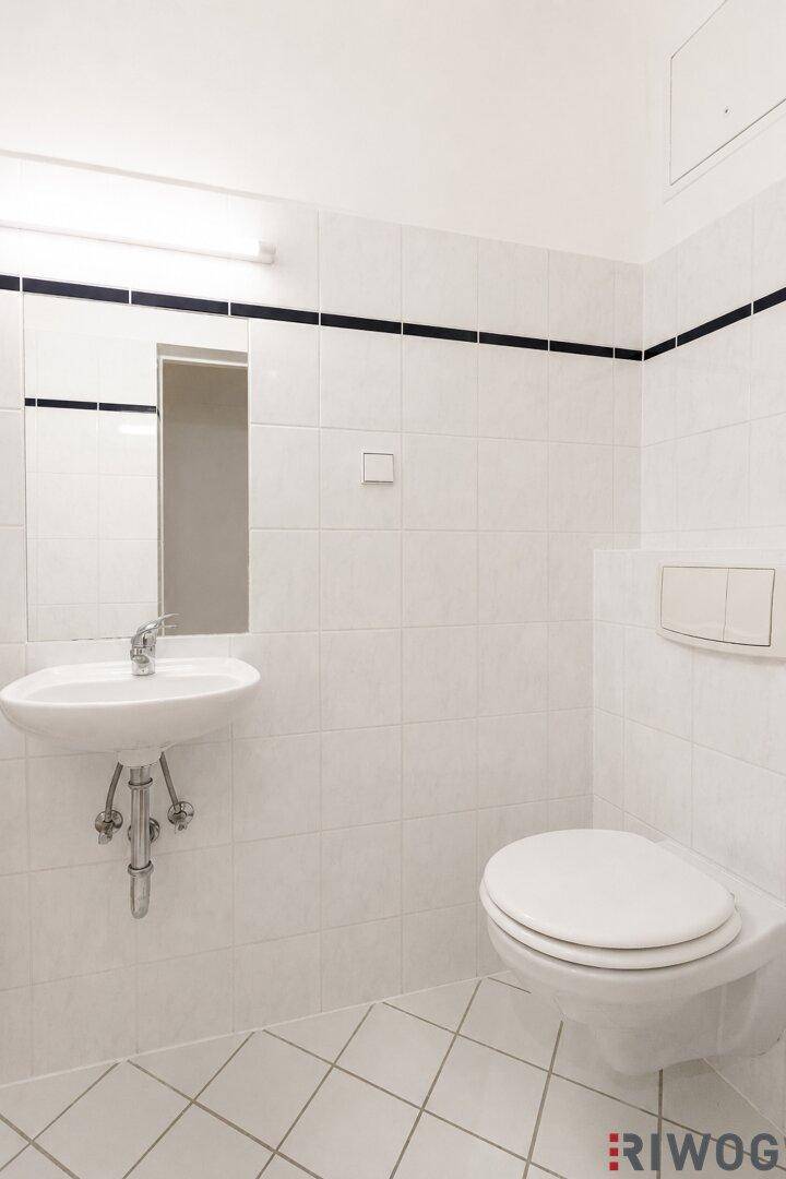 Kleines WC mit weißen Fliesen, wandhängender Toilette und kleinem Waschbecken.