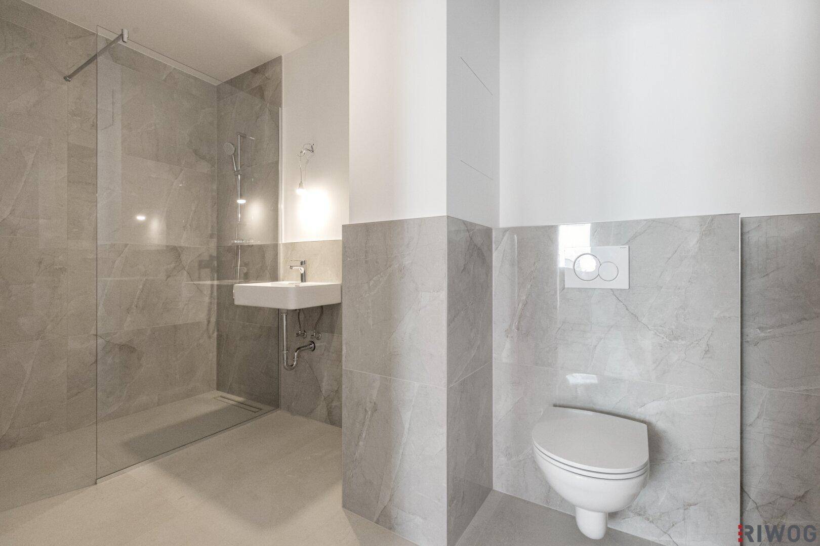 Modernes Badezimmer mit grauen Fliesen, bodengleicher Dusche und wandhängendem WC.