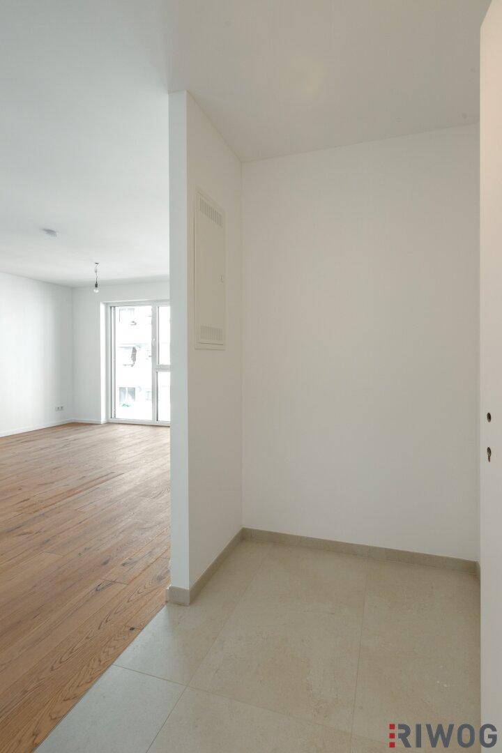 Heller Eingangsbereich mit Fliesenboden, der in einen Raum mit Holzboden übergeht.