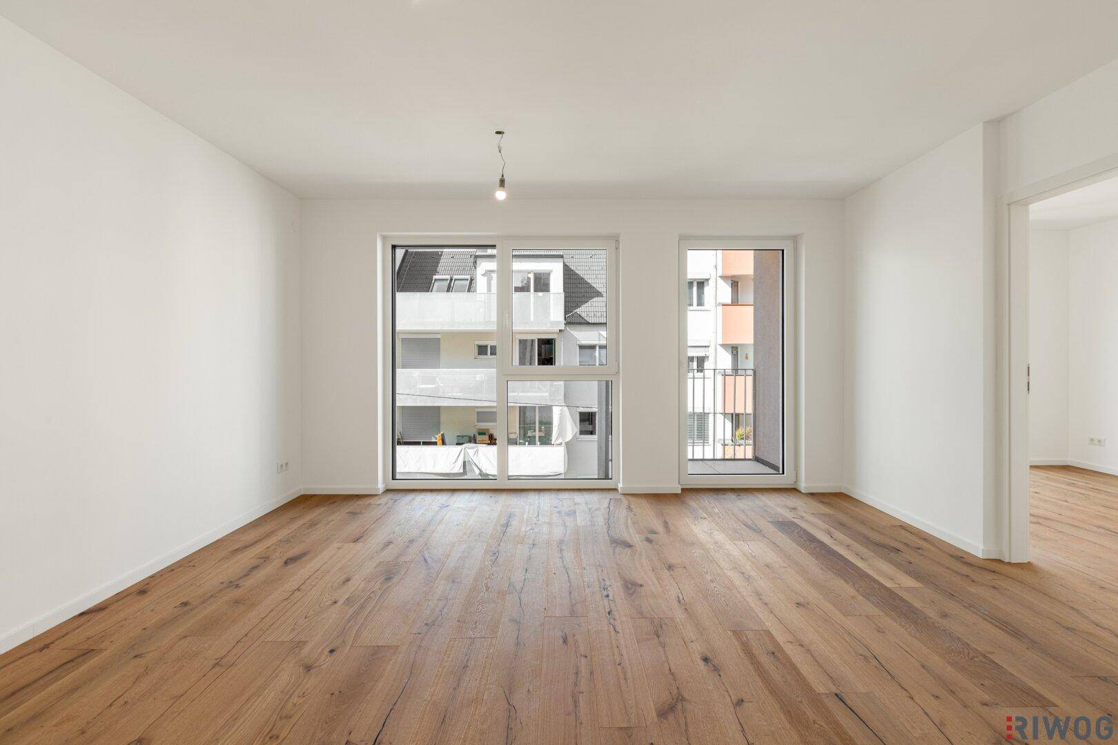 Geräumiges, leeres Wohnzimmer mit Holzboden und großen Fenstern mit Blick auf die Nachbarschaft.