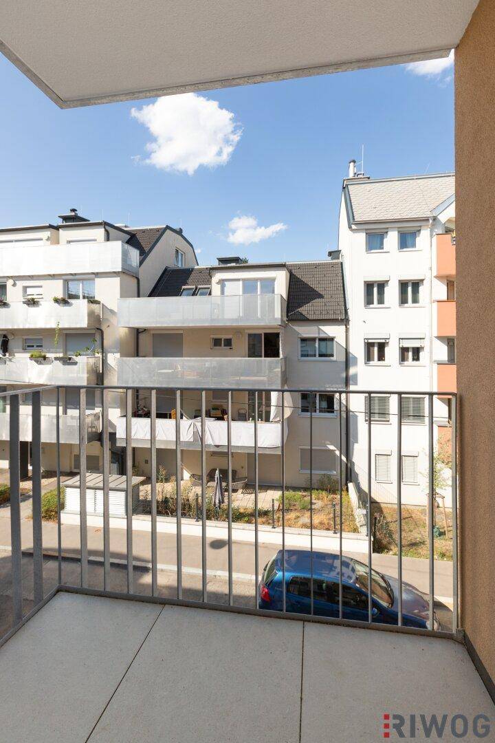 Heller Balkon mit Metallgeländer und Blick auf die umliegenden Gebäude und die Straße.