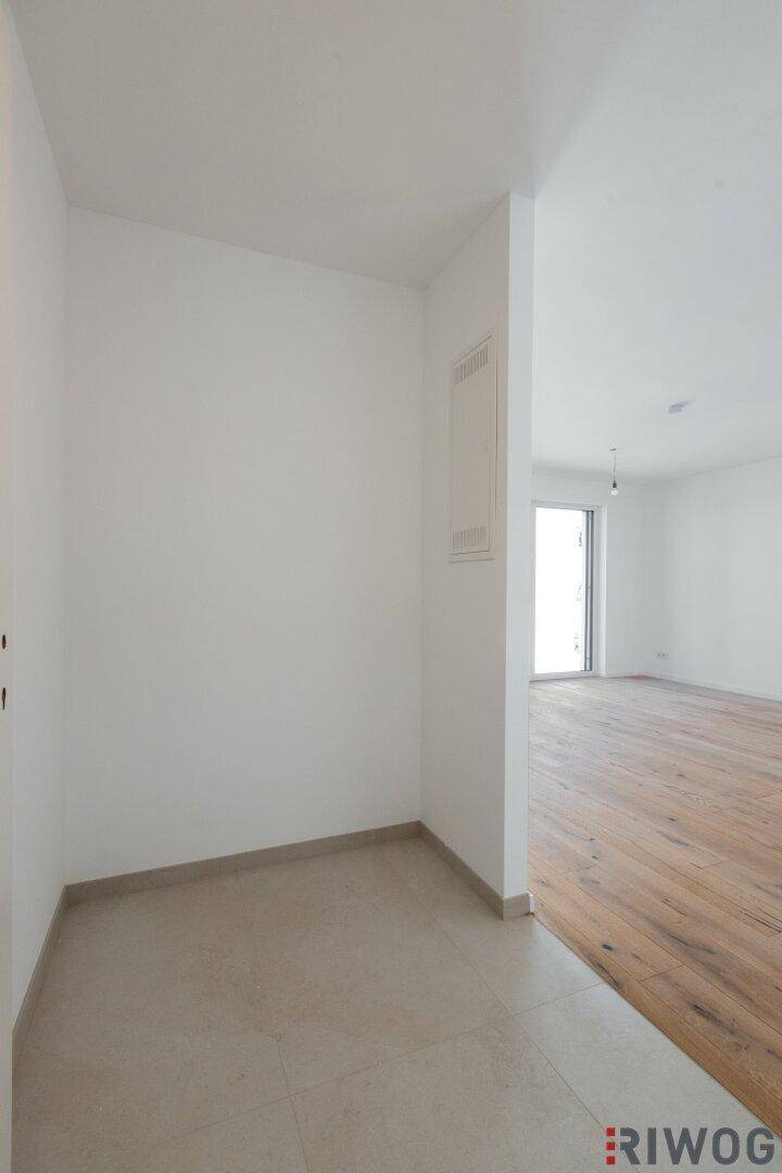Heller Eingangsbereich mit Fliesenboden, der in einen Raum mit Holzboden übergeht.