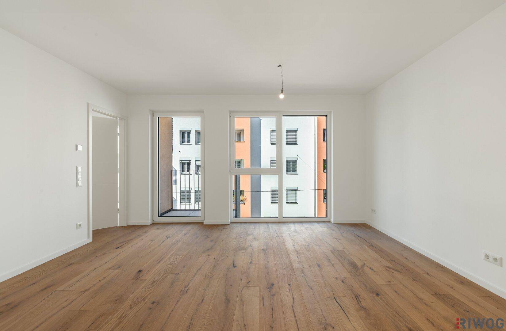 Geräumiges, helles Zimmer mit Holzboden und Zugang zu einem französischen Balkon.