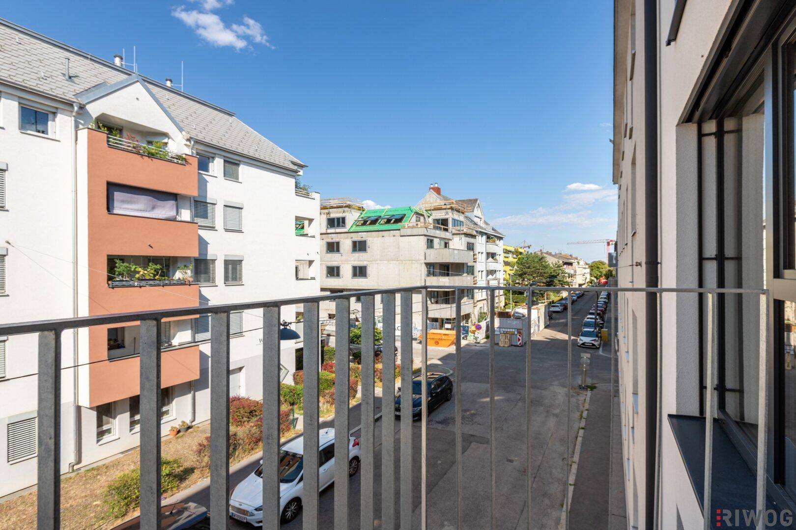 Blick von einem Balkon auf die Straße und umliegende Wohngebäude an einem sonnigen Tag.