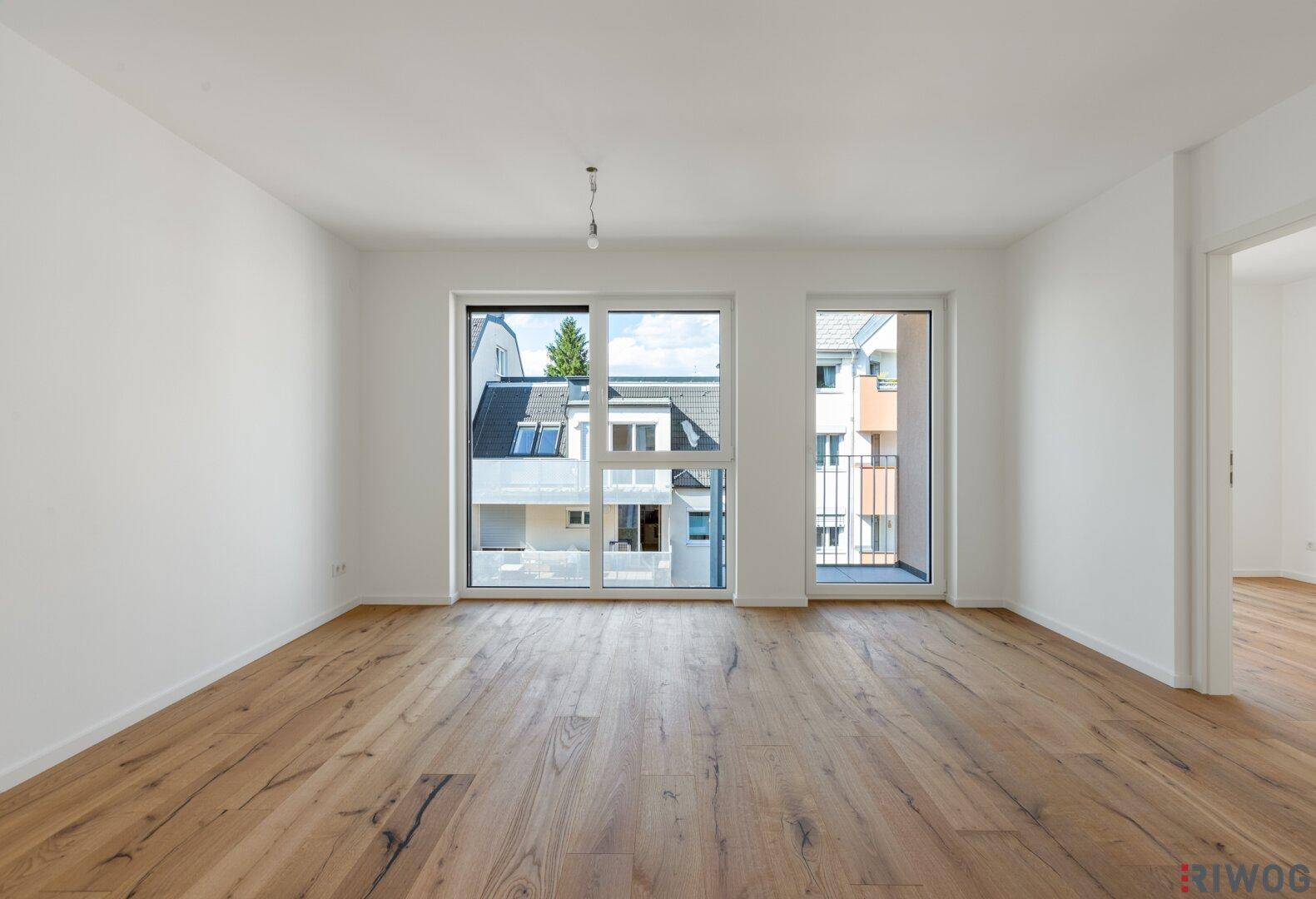 Geräumiges, helles Zimmer mit Holzboden und Zugang zu einem französischen Balkon.
