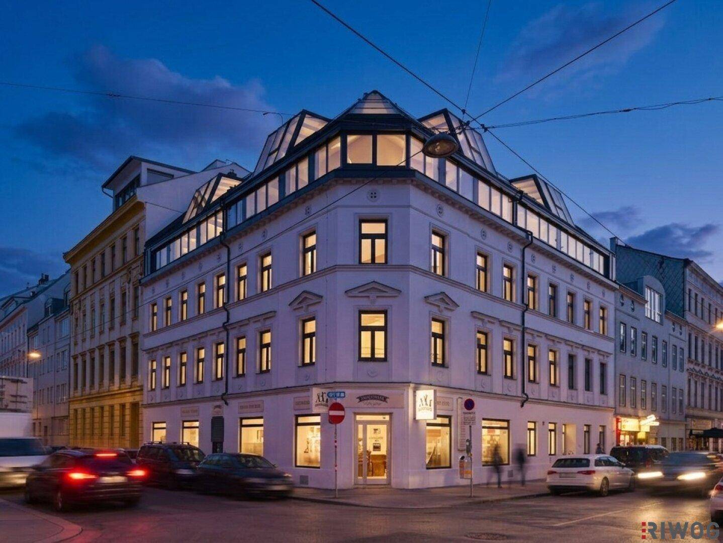 Modernisiertes Eckgebäude in der Stadt bei Dämmerung mit vielen beleuchteten Fenstern und Glasfassade.