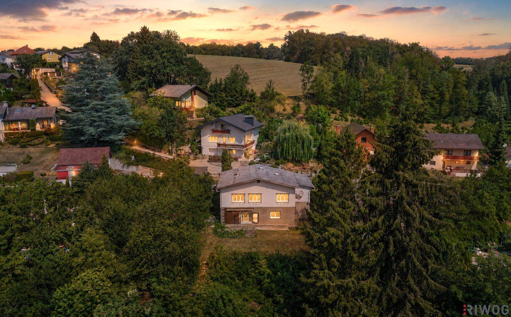 Luftaufnahme einer Wohnsiedlung bei Sonnenuntergang, umgeben von Wald und Feldern.