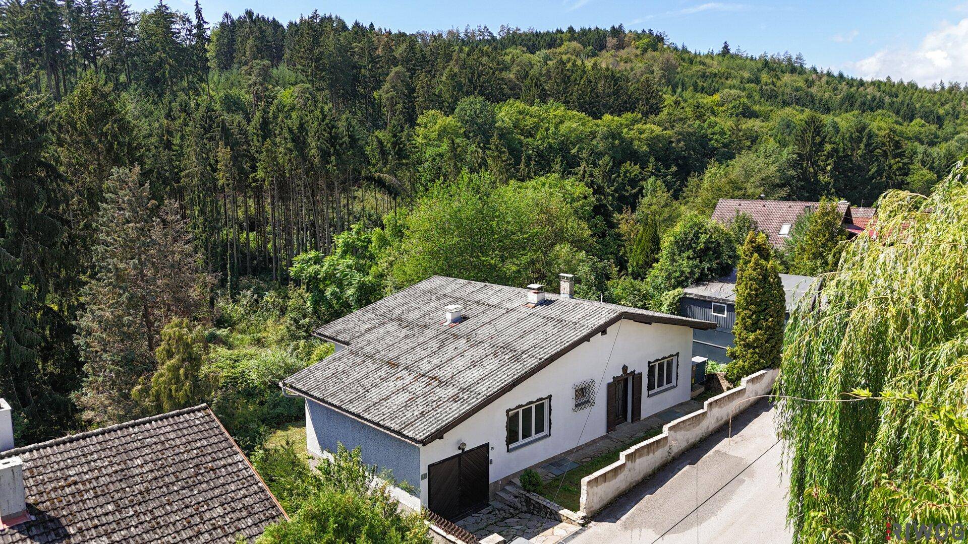 Luftaufnahme eines Hauses mit Satteldach, umgeben von dichtem Wald und Bäumen.