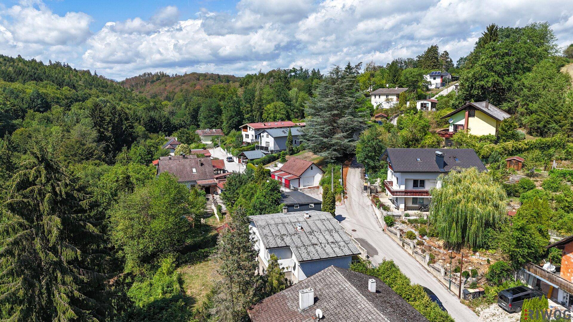 Panoramablick aus der Luft auf eine Wohnsiedlung in einer grünen, hügeligen Landschaft.