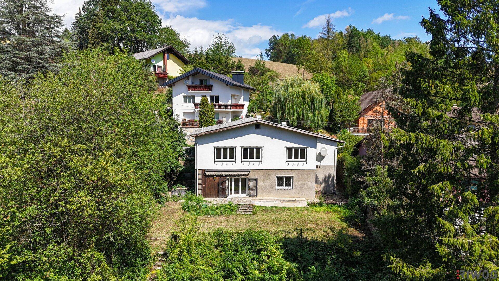 Luftaufnahme eines freistehenden Hauses, eingebettet in eine grüne, bewaldete Umgebung.