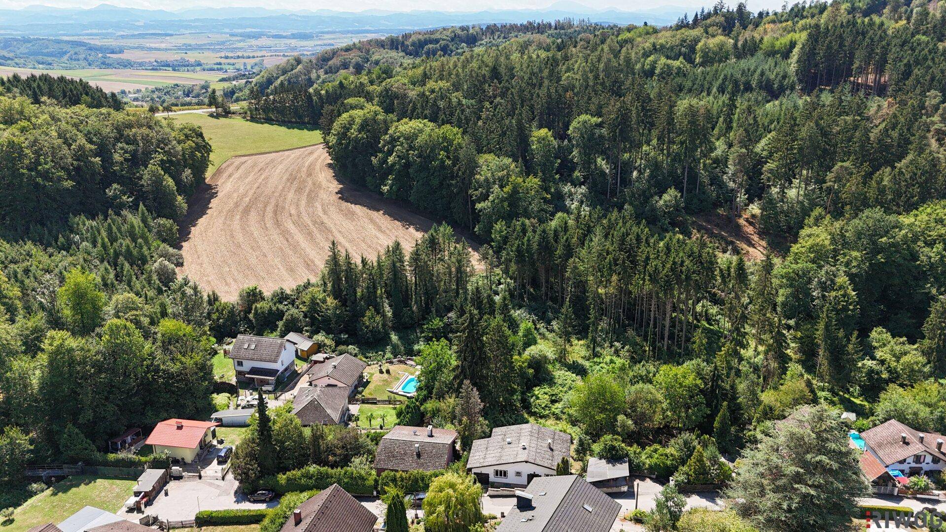 Weitläufige Luftaufnahme einer ländlichen Siedlung, umgeben von Wald und Ackerland.