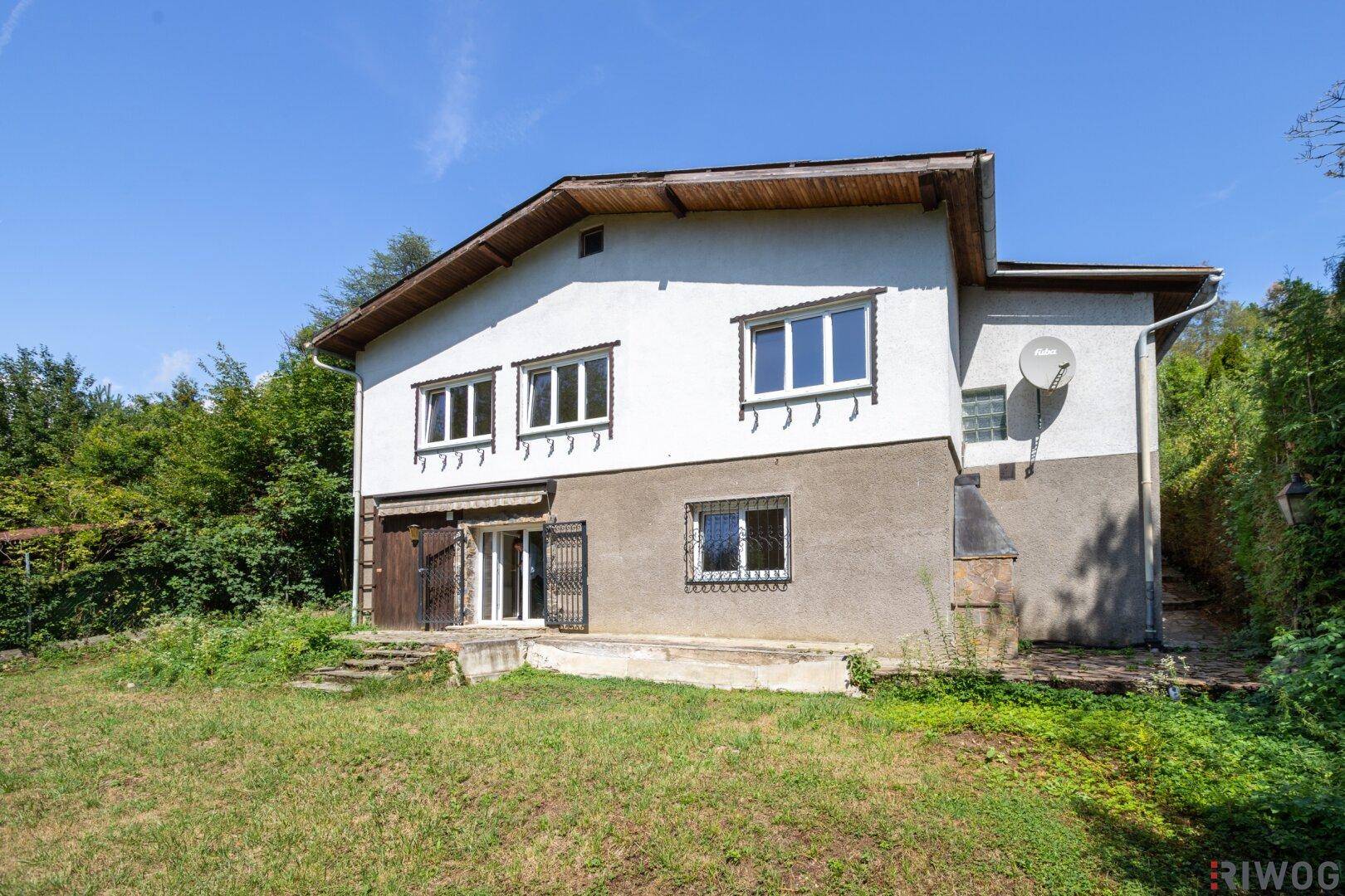 Hausfassade bei Tageslicht mit Garten und umliegender Natur.