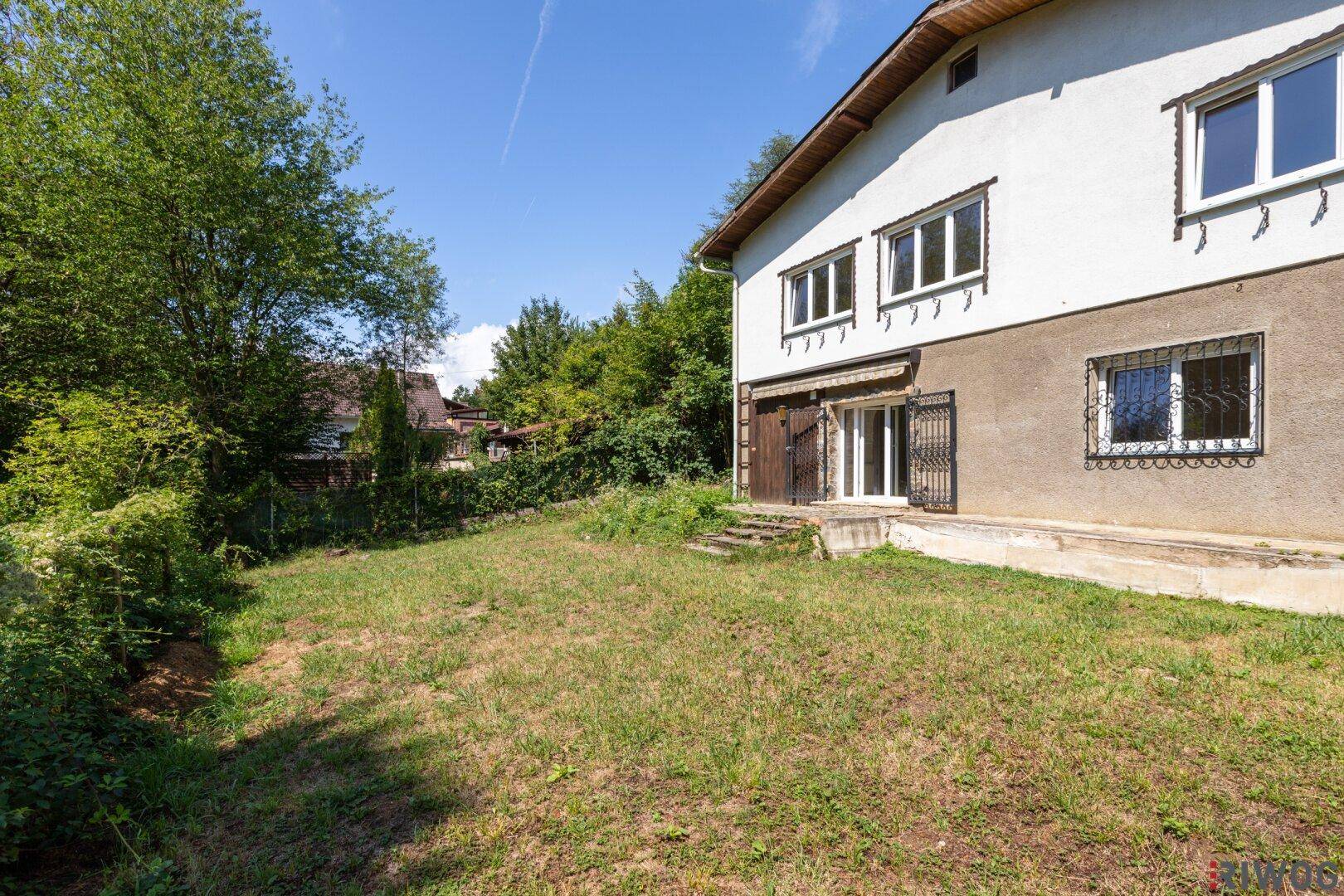 Blick auf den Gartenbereich des Hauses mit Rasenfläche und umgebender Vegetation.