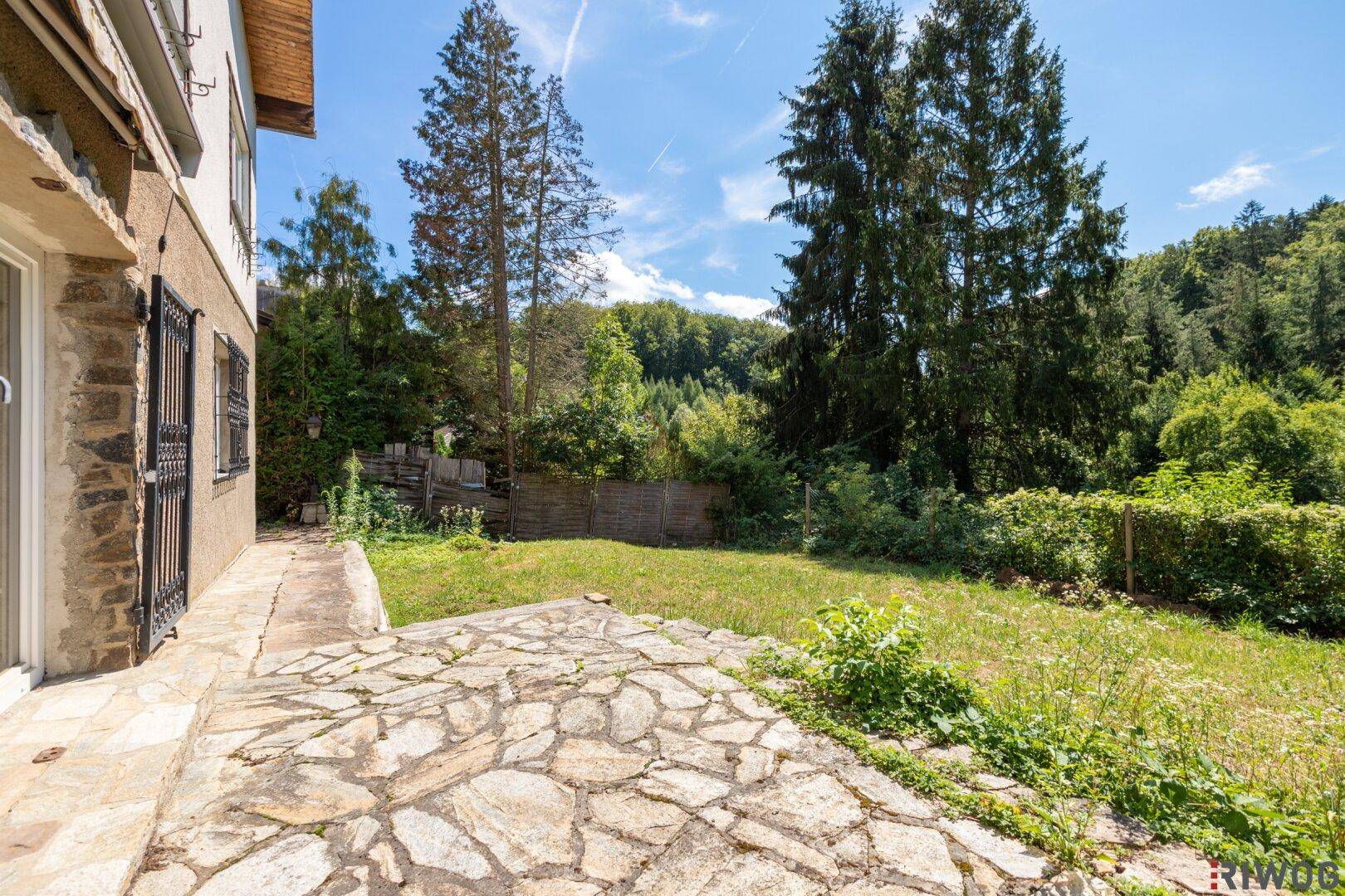 Geräumige Steinterrasse mit Zugang zum Garten und Blick auf die bewaldete Umgebung.