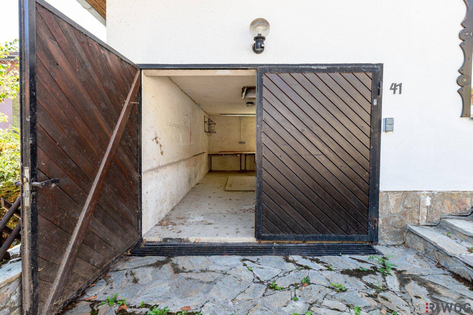 Offene Holzgaragentür führt zu einem leeren Lagerraum mit steinernem Vorplatz und Hausnummer 41.