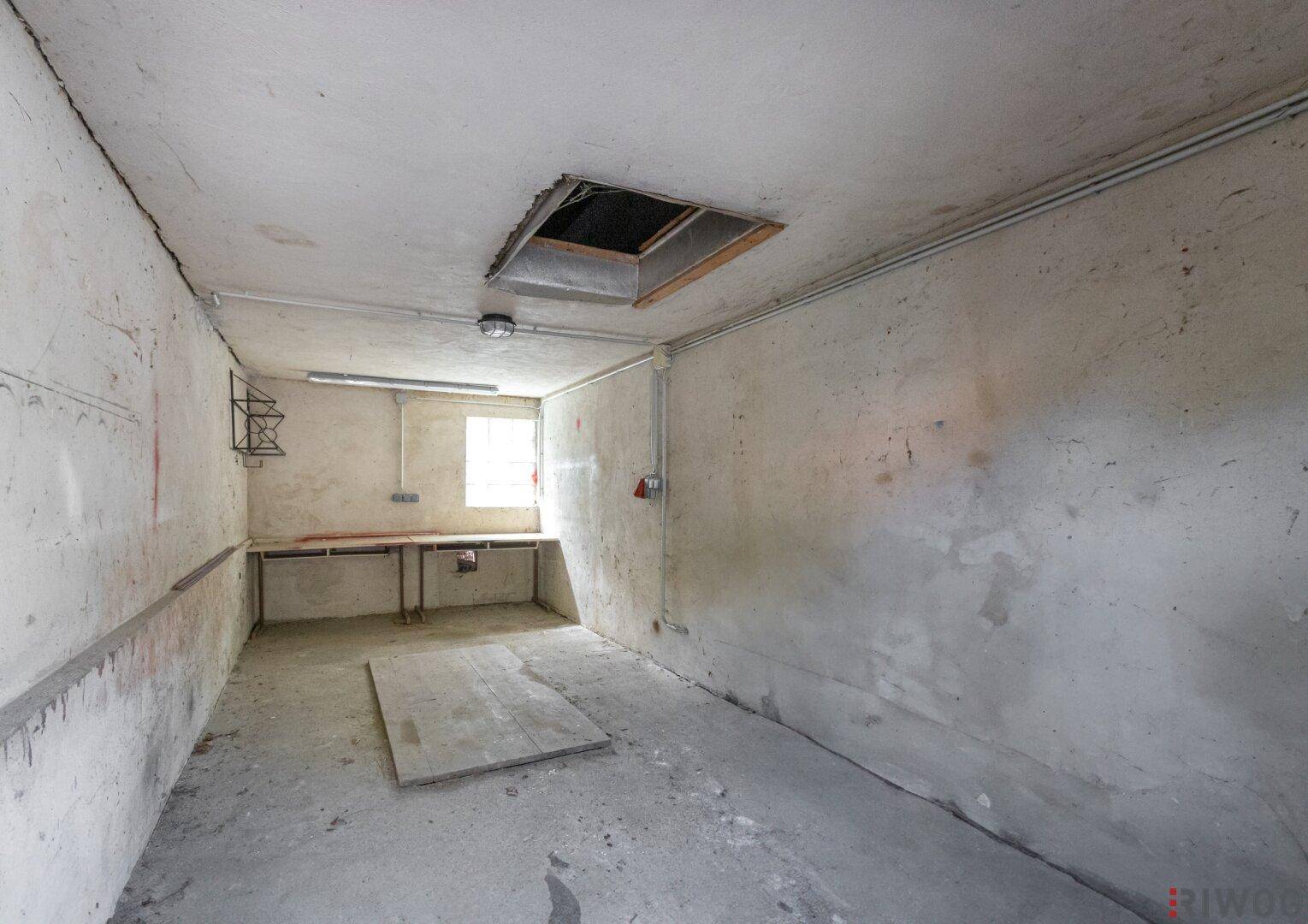 Leerer, unfertiger Lagerraum mit Betonboden, rauen Wänden und einem kleinen Fenster für Tageslicht.