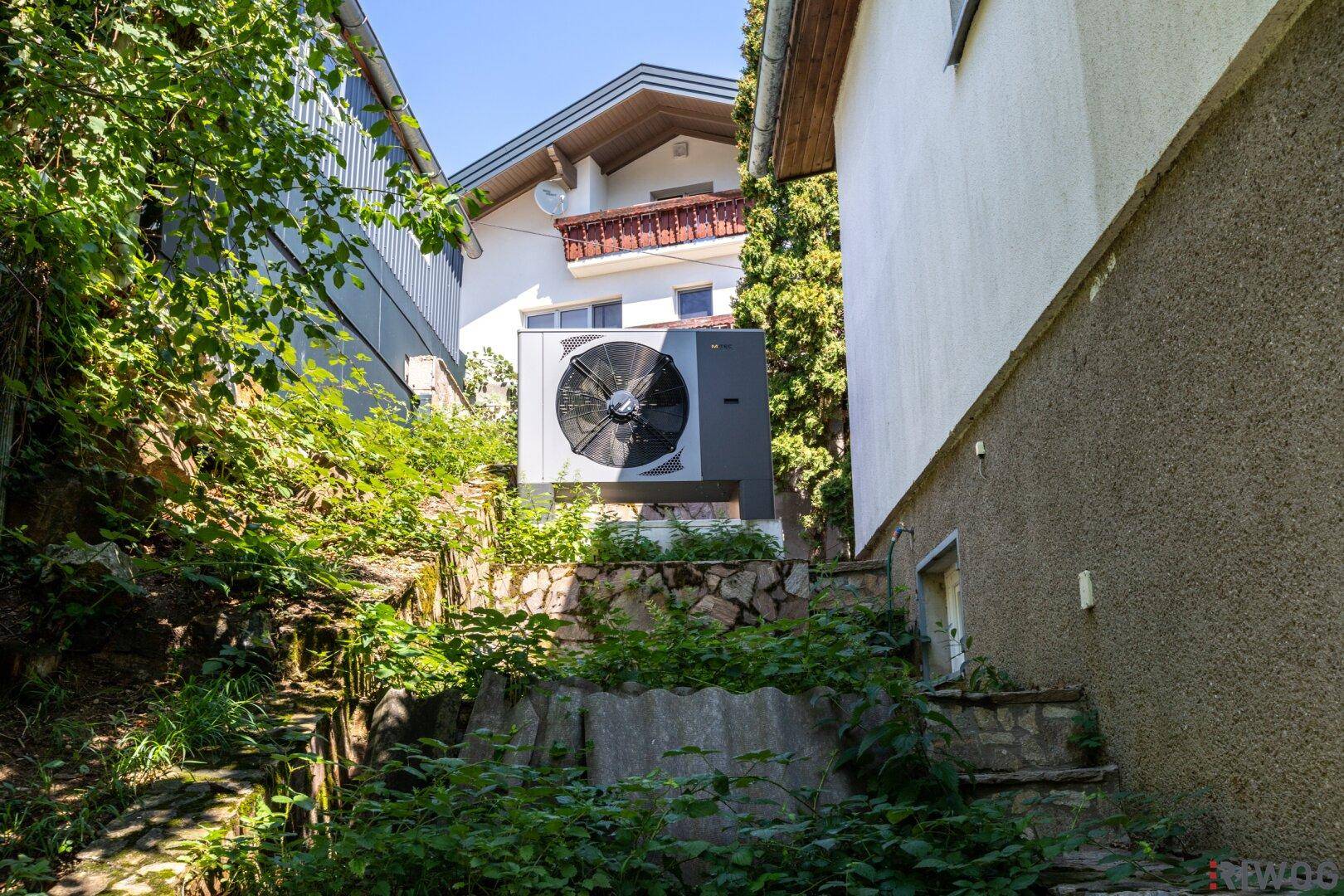 Wärmepumpe im Außenbereich des Hauses, umgeben von Vegetation.