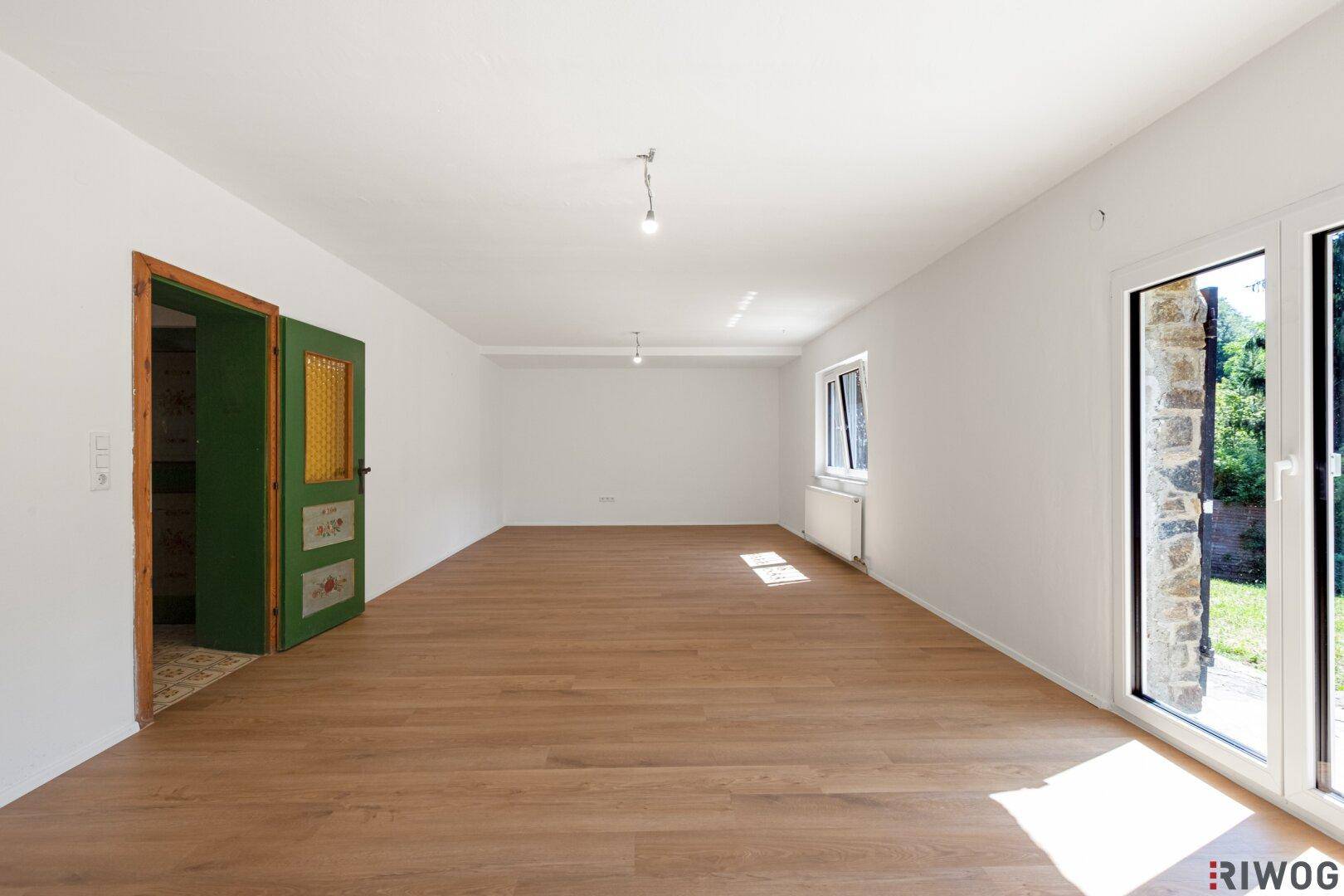 Geräumiges, leeres Zimmer mit Laminatboden und Zugang zum Gartenbereich.