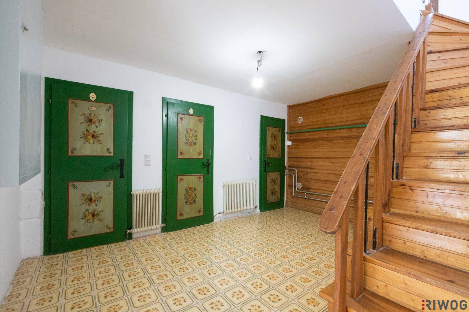Flur mit gemusterten Fliesen, Holztreppe und traditionell bemalten grünen Türen.