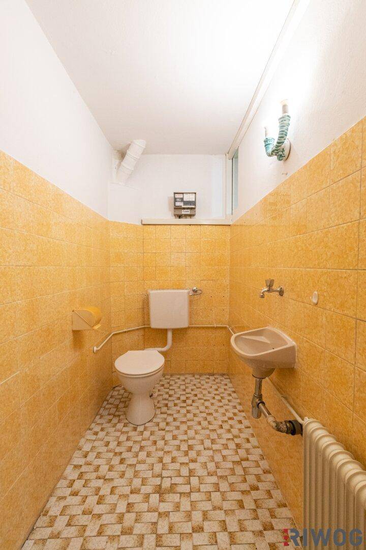 Kleines WC mit gelben Fliesen, Toilette, Waschbecken und Heizkörper.
