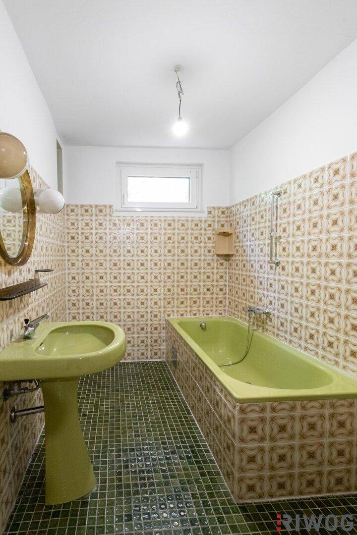 Badezimmer im Retro-Stil mit grüner Badewanne, Waschbecken und gemusterten Fliesen.