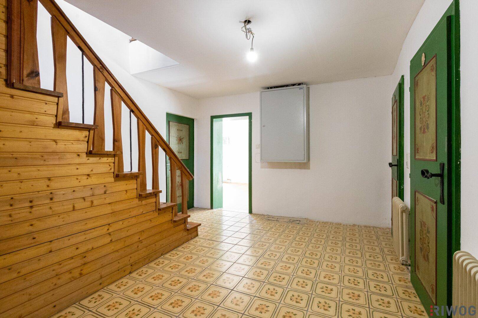 Flur mit Holztreppe, gemusterten Fliesen und traditionell bemalten grünen Türen.