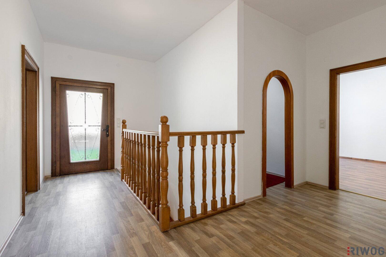 Heller Flur mit Holzboden, Holzgeländer und einer Holztür mit Glaseinsatz.