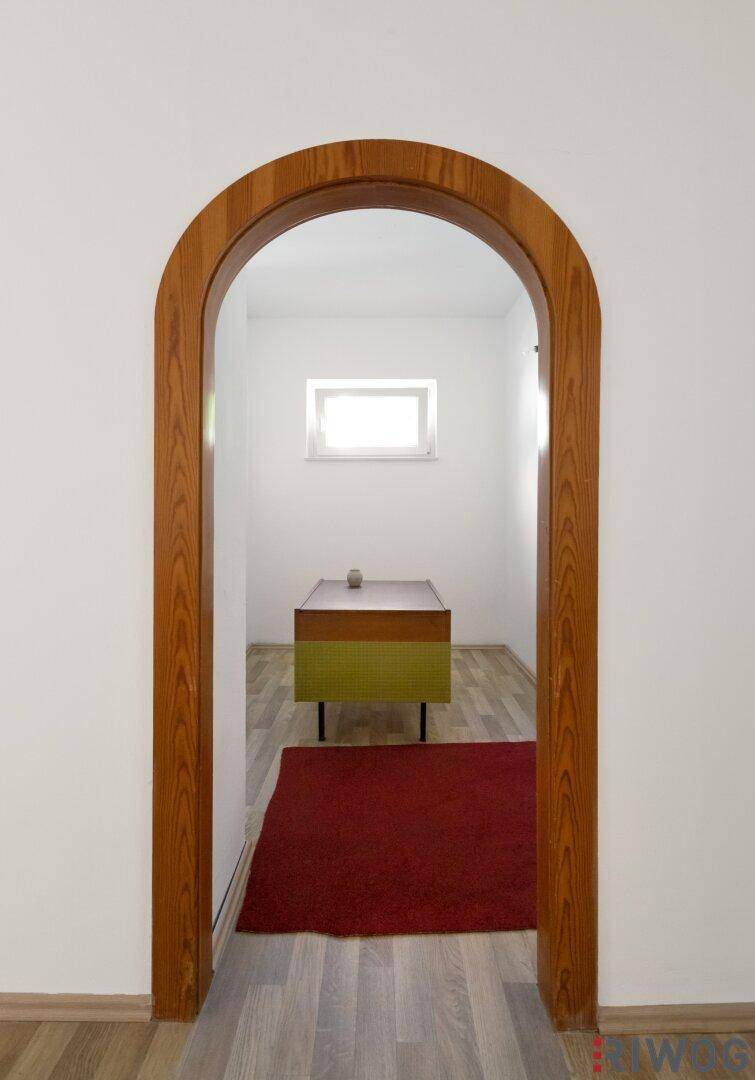 Blick durch einen Holz-Rundbogen in einen Raum mit Holzboden und kleinem Fenster.