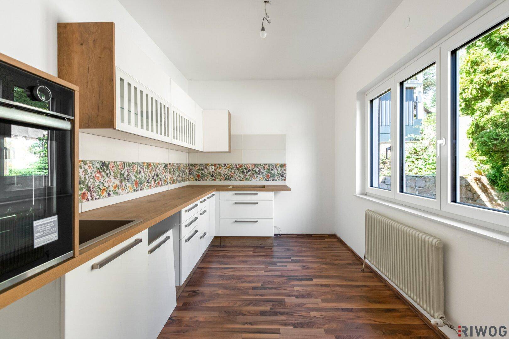 Helle Küche mit weißen Schränken, Holzarbeitsplatten und floraler Rückwand.