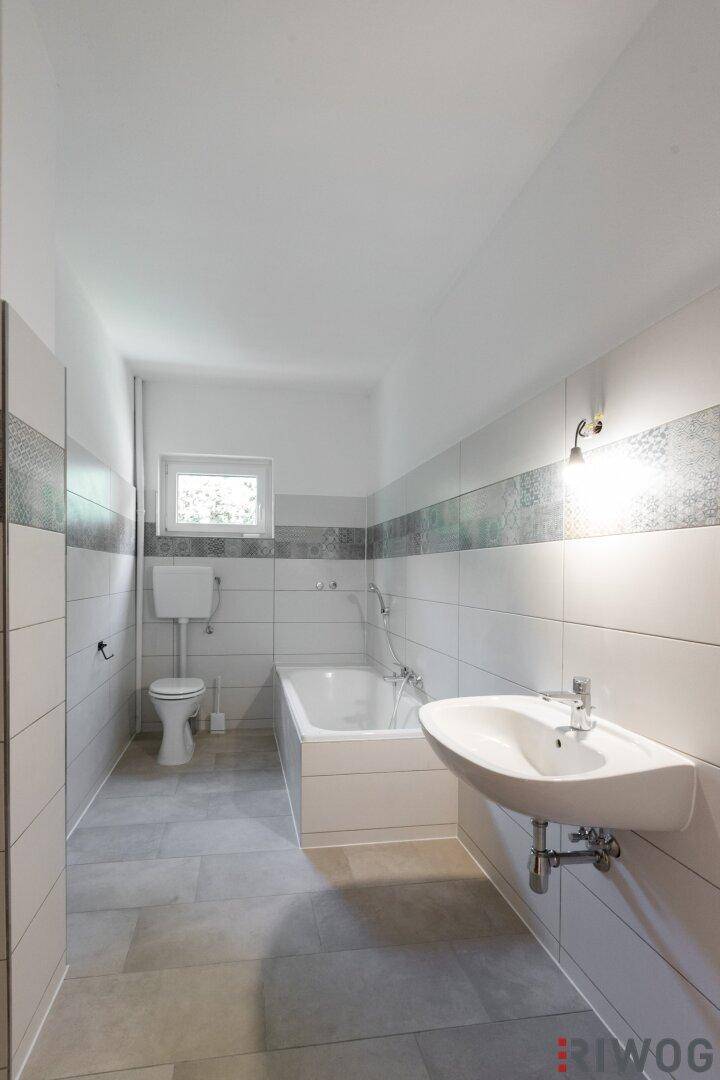 Modern gefliestes Badezimmer mit Badewanne, Toilette, Waschbecken und Fenster.