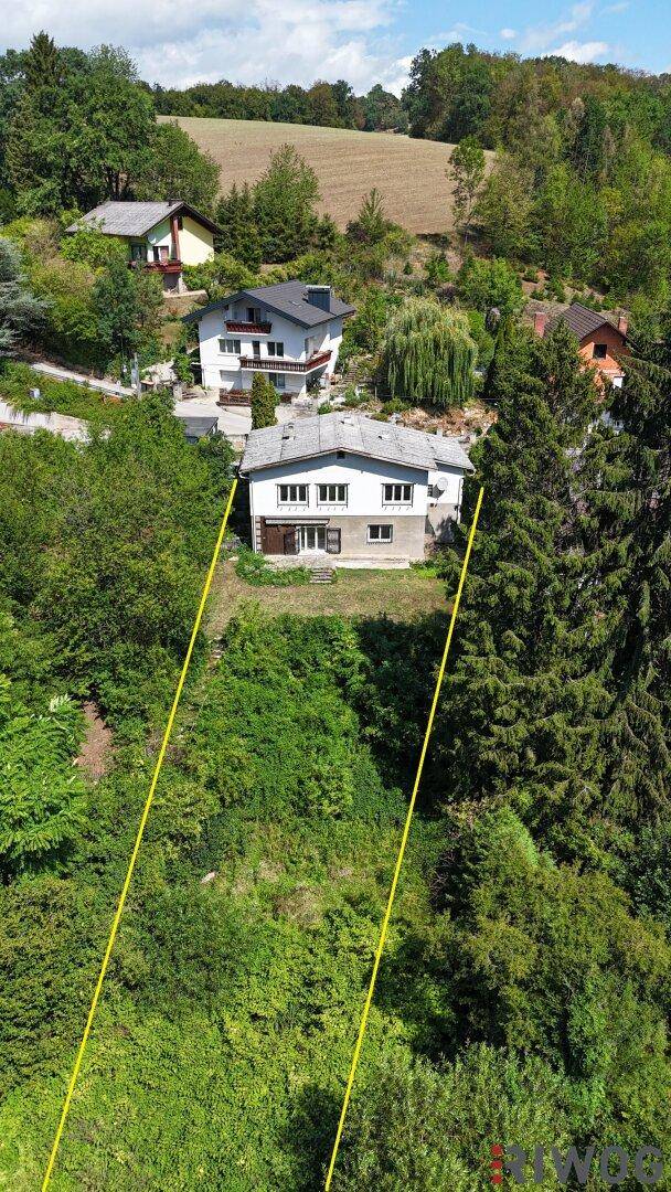 Luftaufnahme eines Hauses mit Grundstücksgrenzen, umgeben von viel Grün und Bäumen.