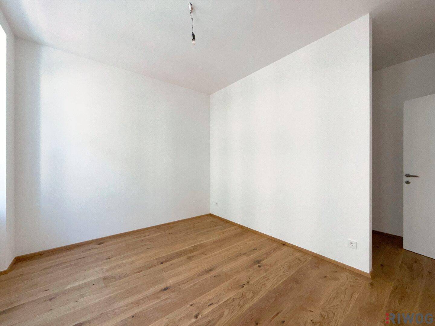 Leeres Schlafzimmer mit hellem Holzfußboden und weißen Wänden, bereit zum Einzug.