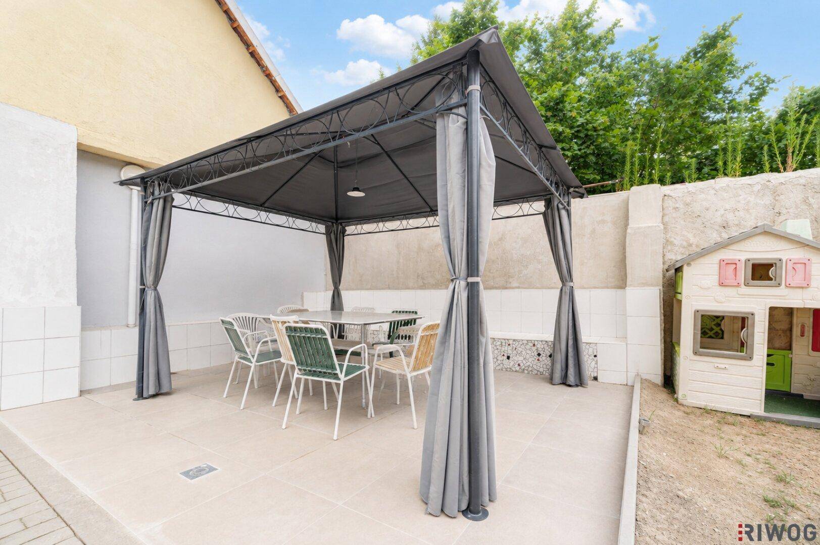 Gepflasterte Terrasse mit Pavillon, Esstisch und Kinderspielhaus im Freien.