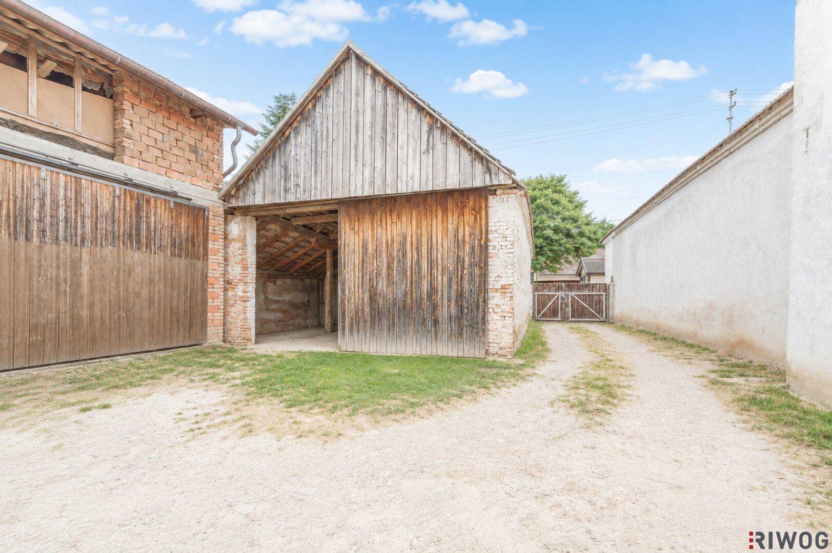 Alte Scheune mit großen Holztoren und Schotterzufahrt auf dem Grundstück.