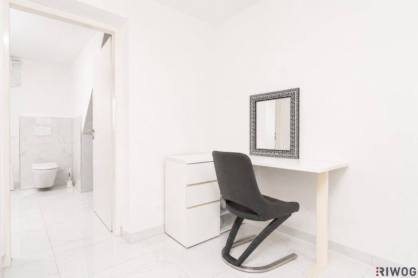 Heller Flur mit weißem Schreibtisch und Blick in ein modernes Badezimmer mit Wand-WC.