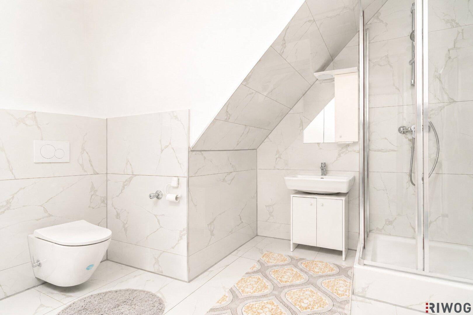 Modernes Badezimmer im Dachgeschoss mit weißen Fliesen, Dusche und Wand-WC unter der Dachschräge.