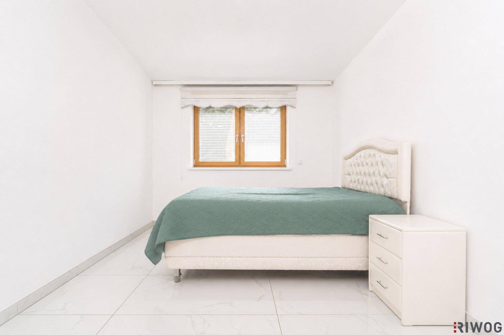 Helles Schlafzimmer mit weißem Fliesenboden, beigem Bett und einem Fenster mit Jalousien.