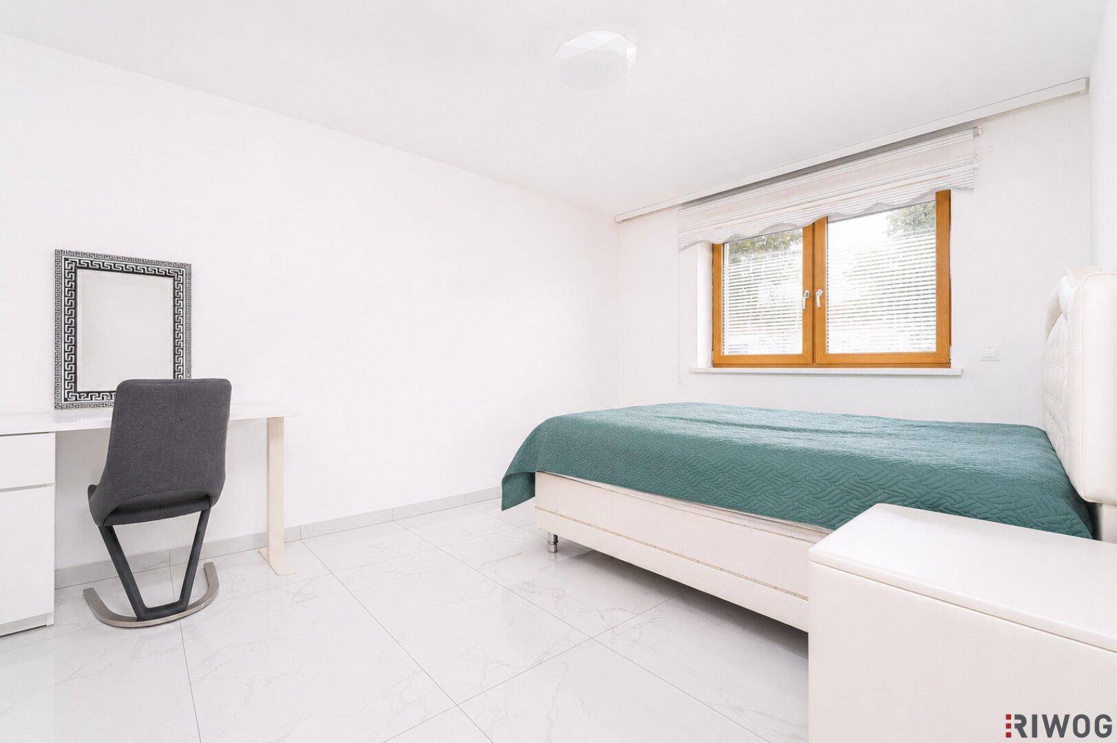 Geräumiges Schlafzimmer mit weißem Fliesenboden, beigem Bett, Schreibtisch und Fenster mit Jalousien.