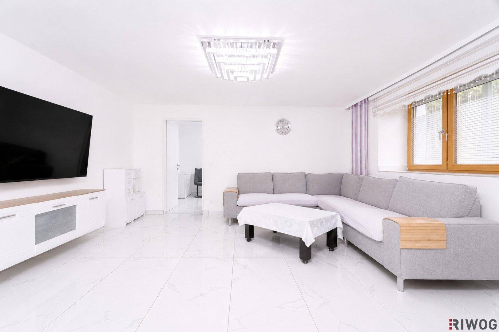 Helles Wohnzimmer mit großem Ecksofa, Fliesenboden und einem modernen Deckenlicht.
