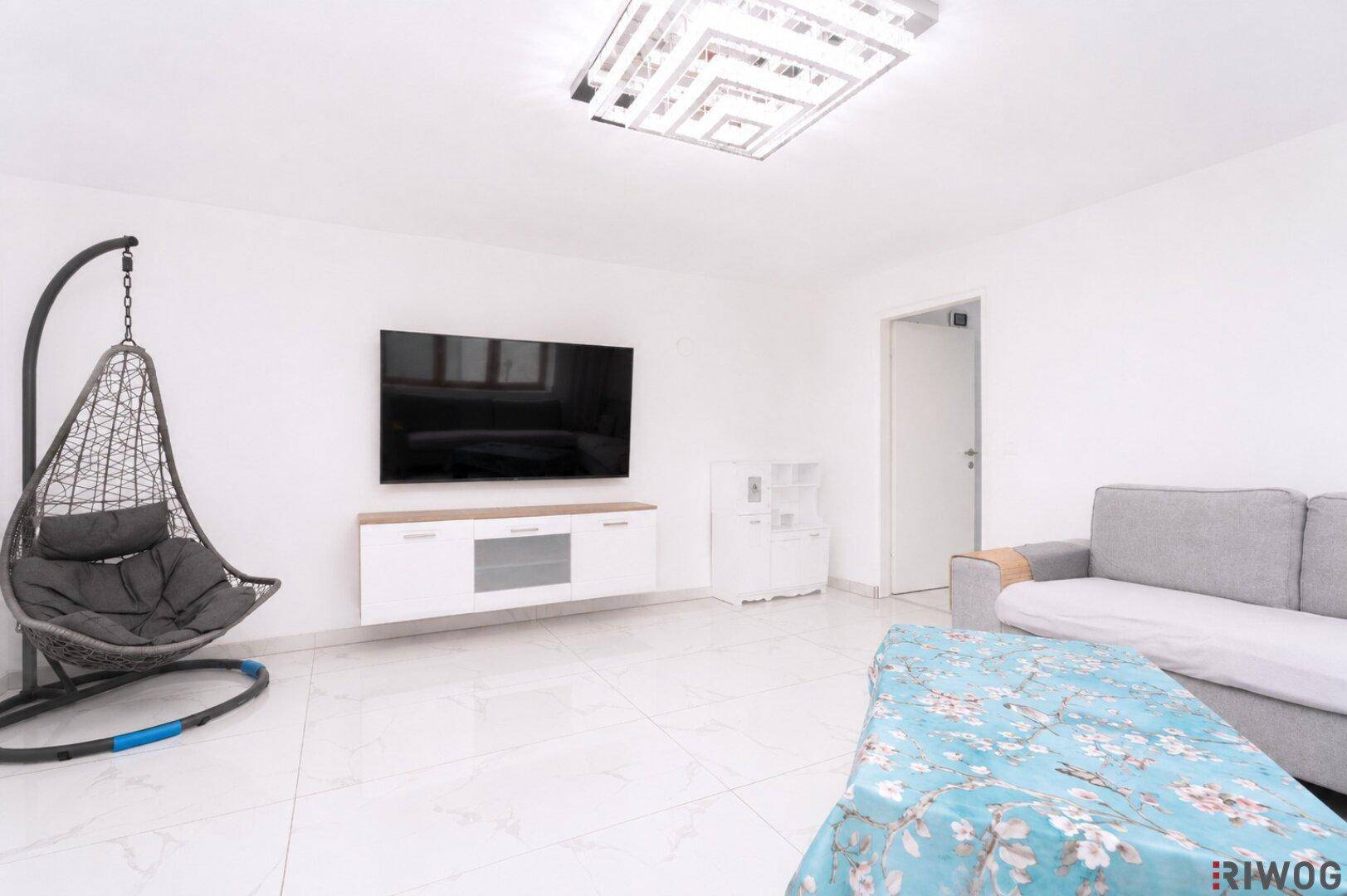 Modernes Wohnzimmer mit Hängesessel, großem Fernseher und weißem Fliesenboden.
