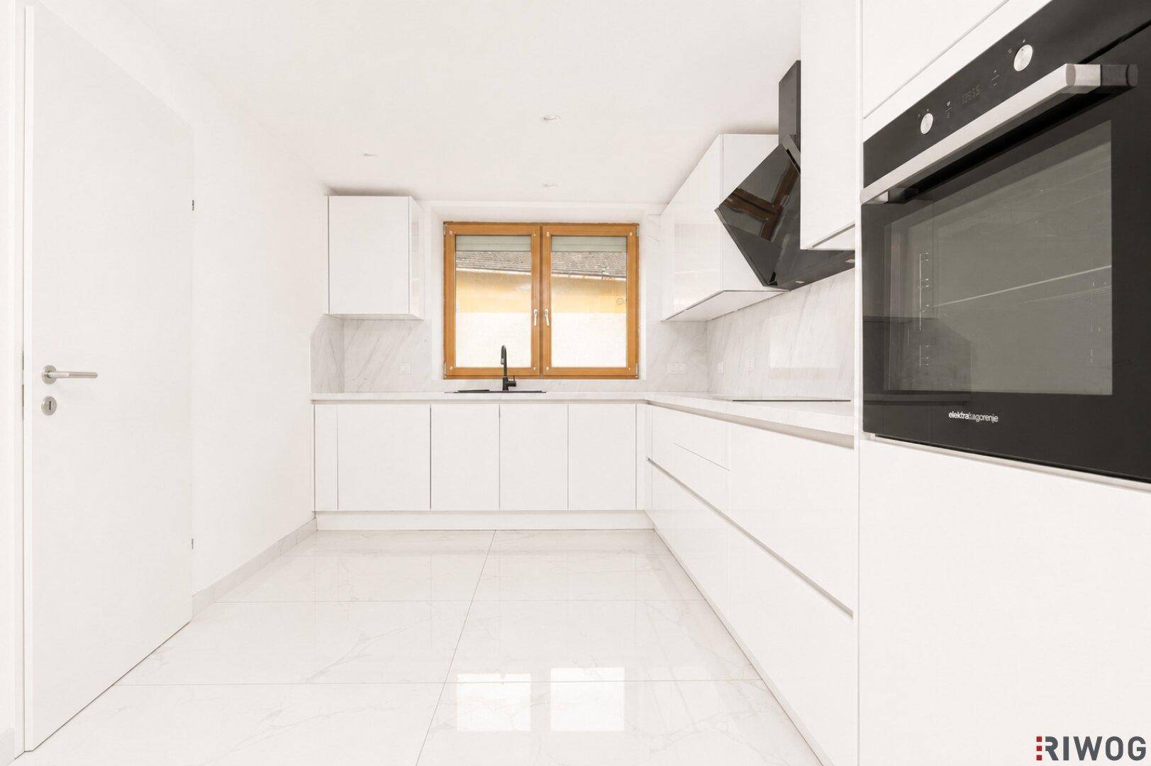 Moderne weiße Küche mit Hochglanzfronten, Einbaugeräten und Fenster mit Jalousien.