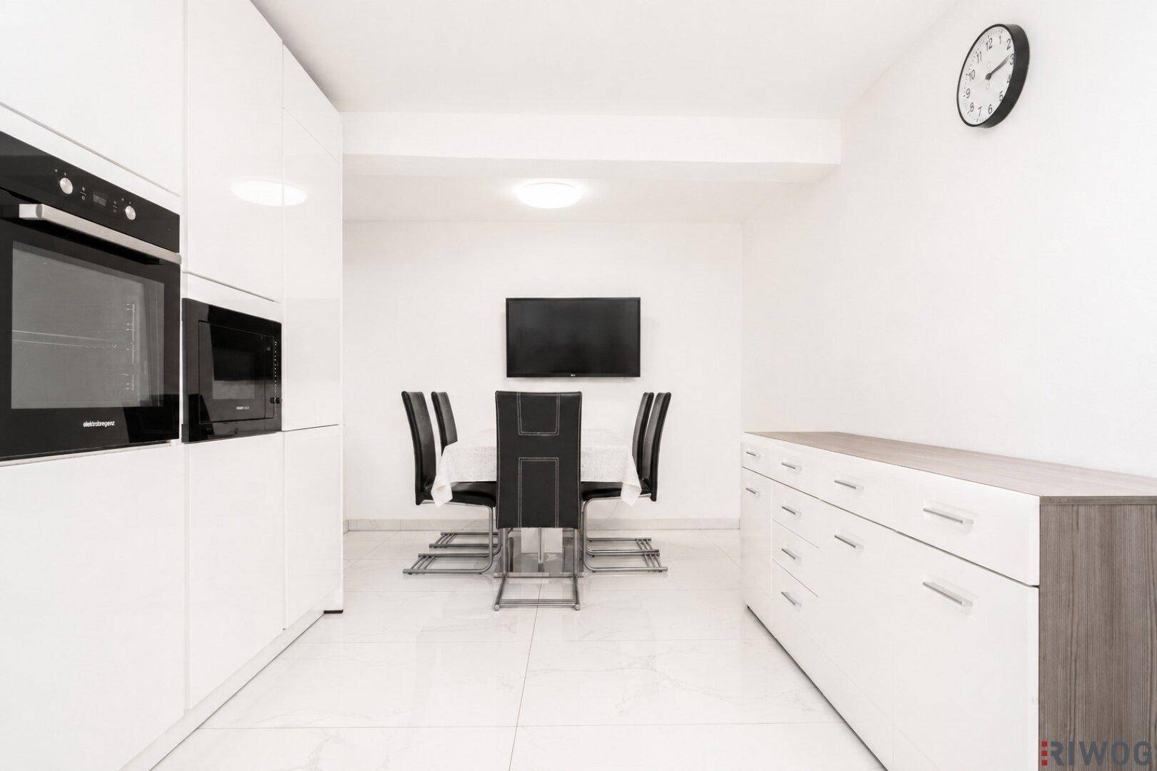 Moderne weiße Küche mit Essbereich, Einbaugeräten und einem Sideboard.