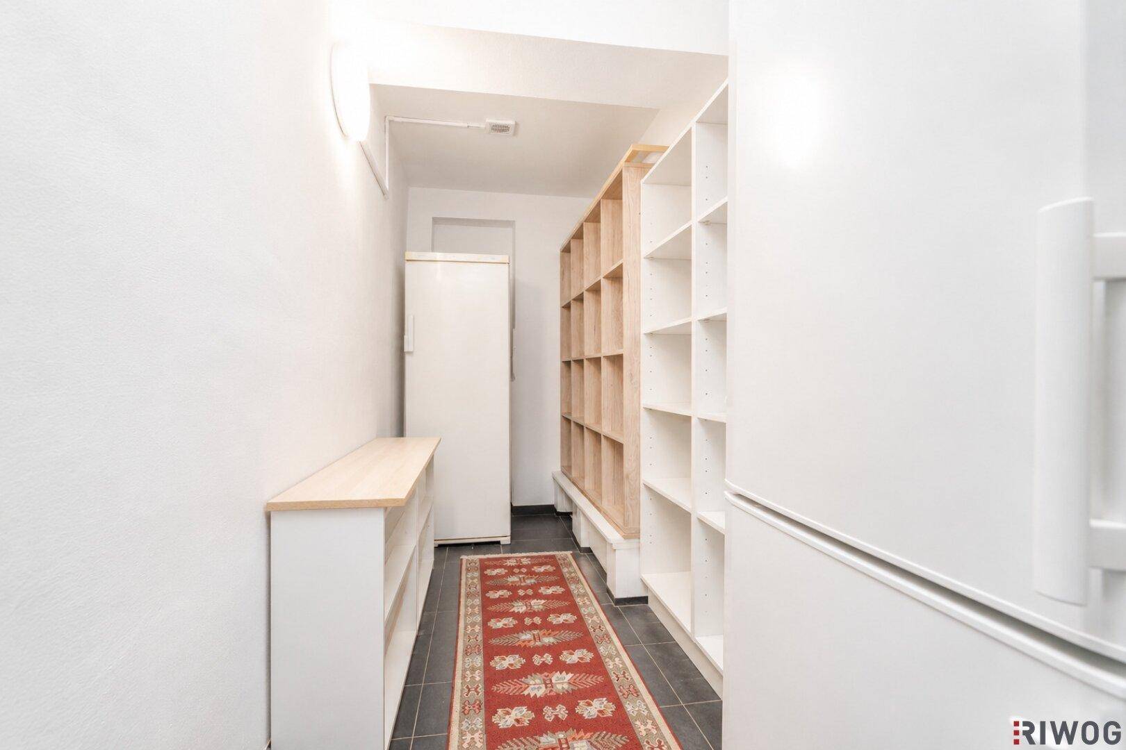 Langer Abstellraum mit Regalen, weißem Schrank und dunklem Fliesenboden.