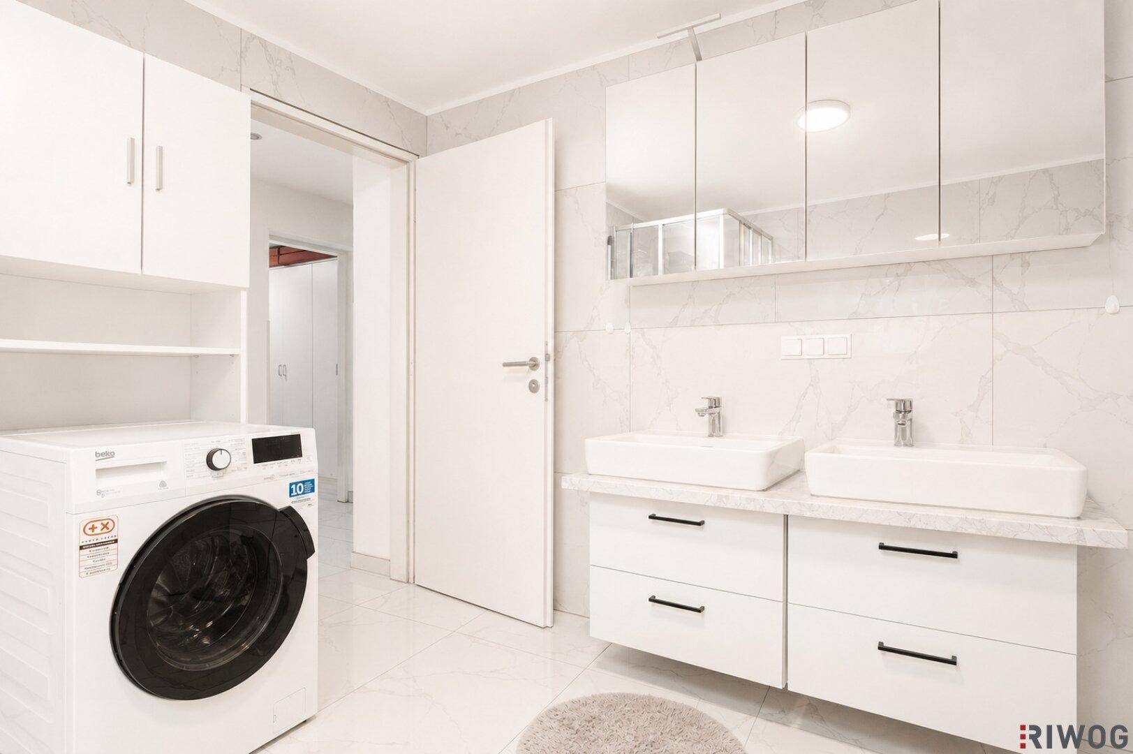 Modernes Badezimmer mit Doppelwaschbecken, Waschmaschine und Spiegelschrank.