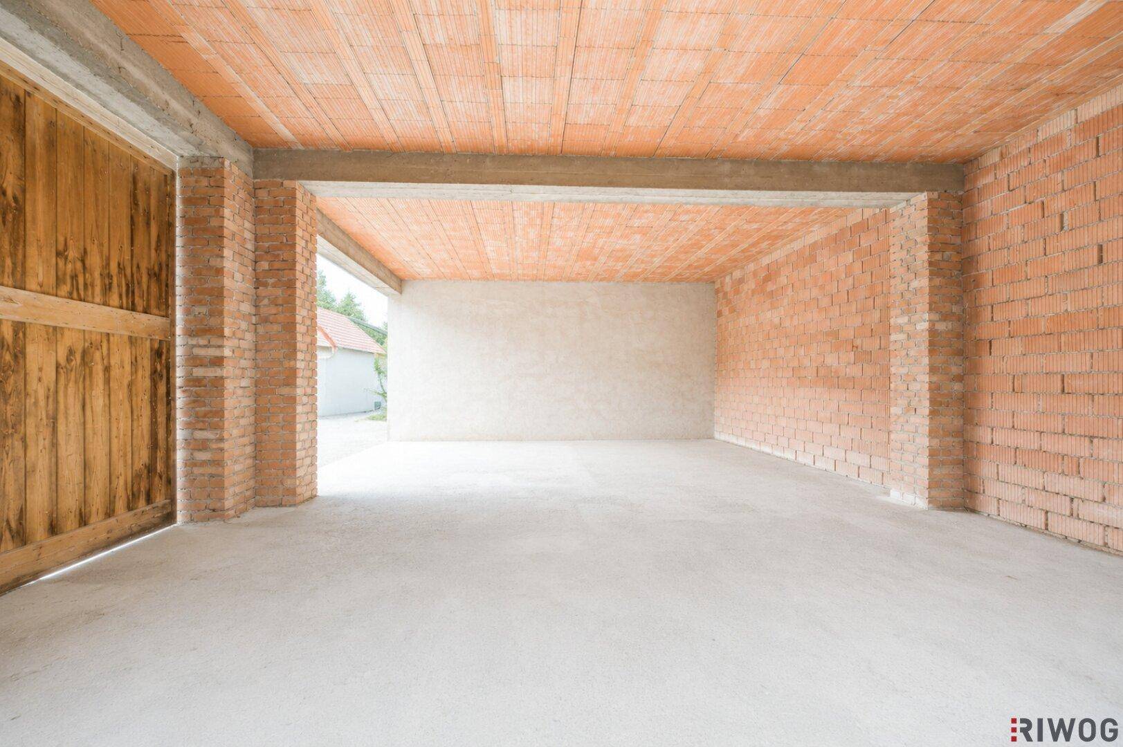 Unfertige Garage mit Ziegelwänden und Betonboden, bereit für den Ausbau.