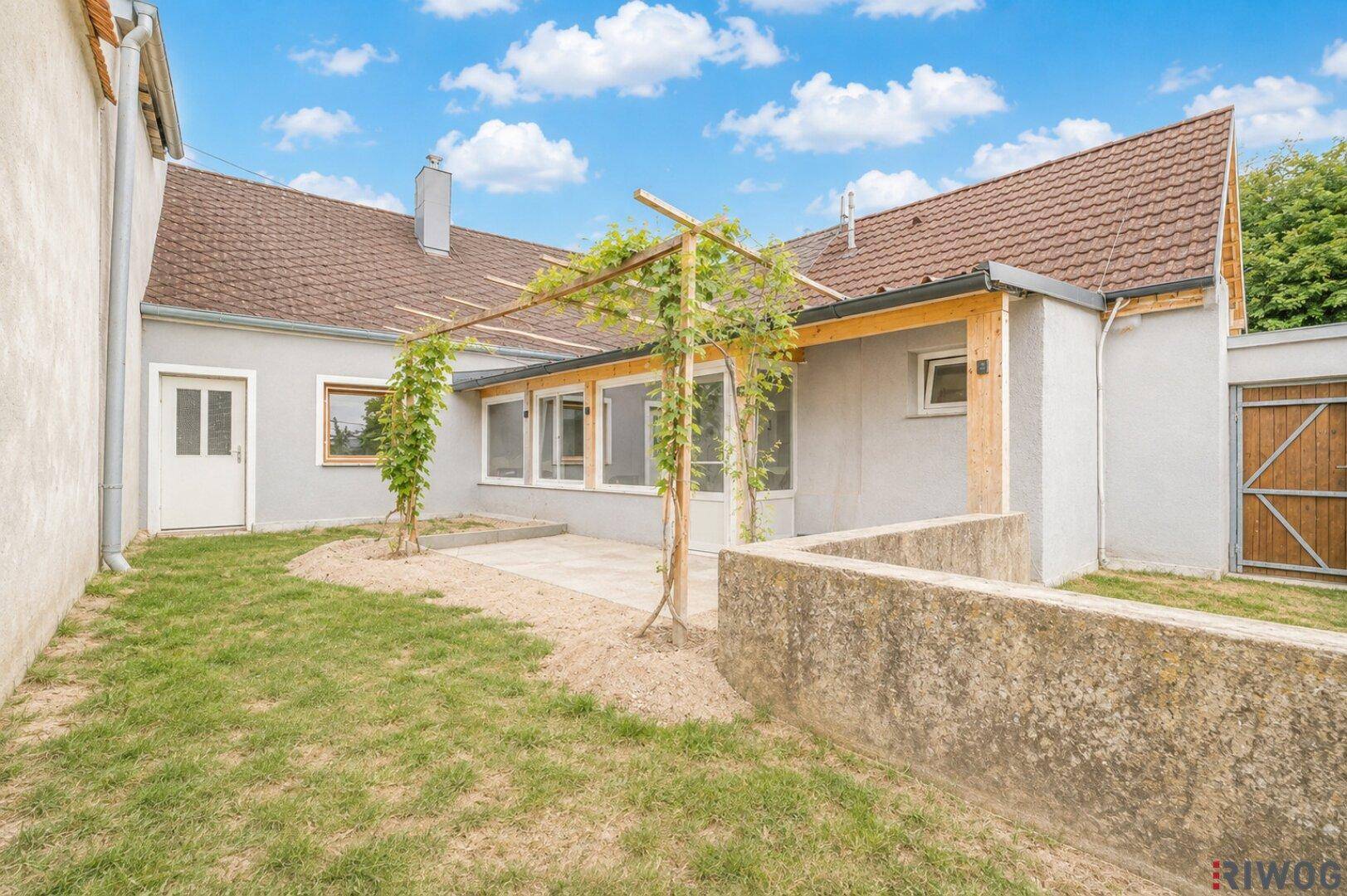 Gepflegter Garten mit Terrasse, Pergola und Grünflächen hinter dem Haus.