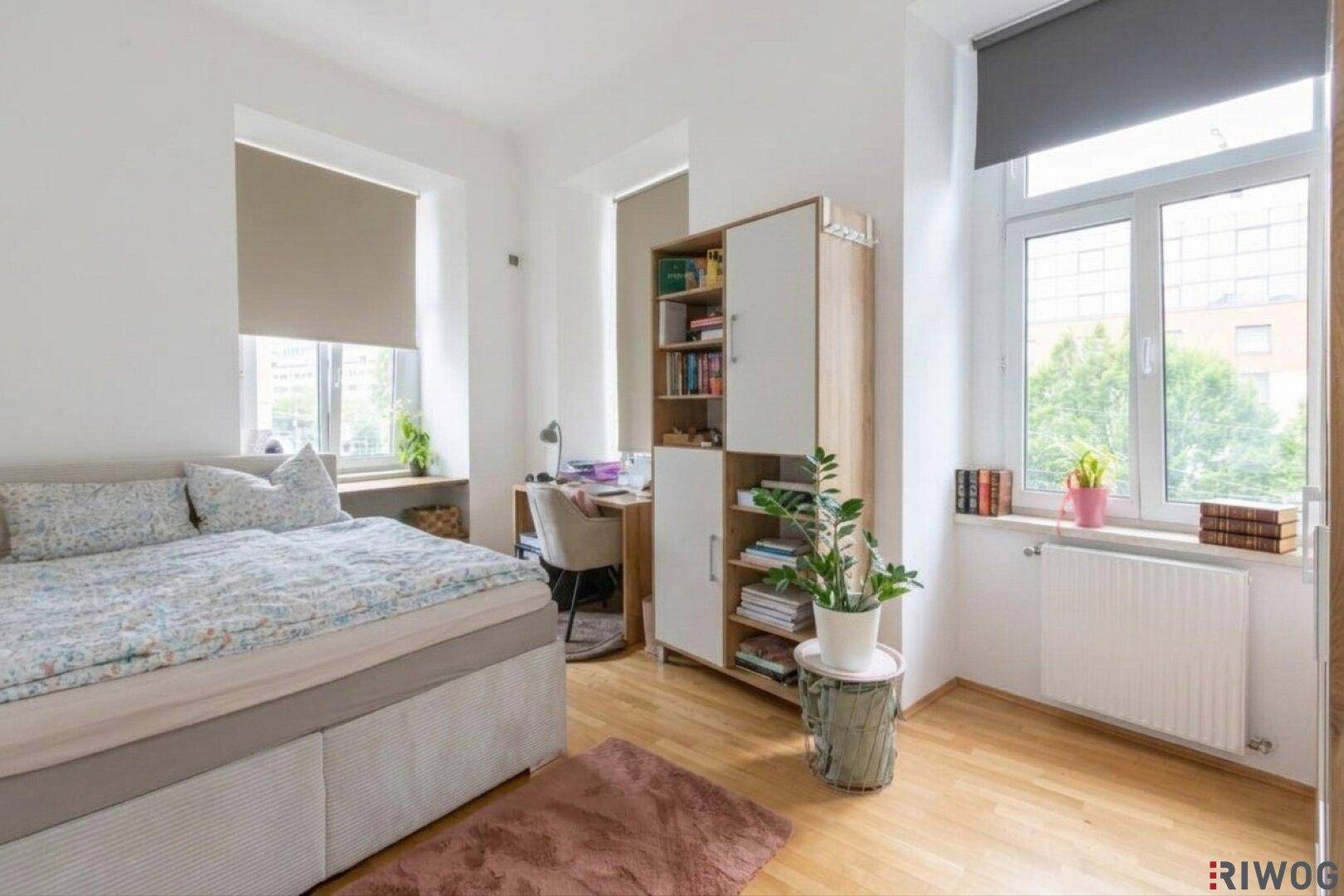 Helles Schlafzimmer mit Holzboden, großem Bett und Schreibtisch am Fenster.