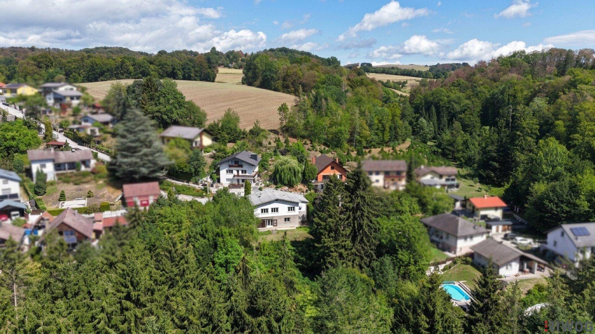 Panoramablick auf eine Wohnsiedlung in sonniger, grüner Landschaft mit einem Pool und weitem Horizont.