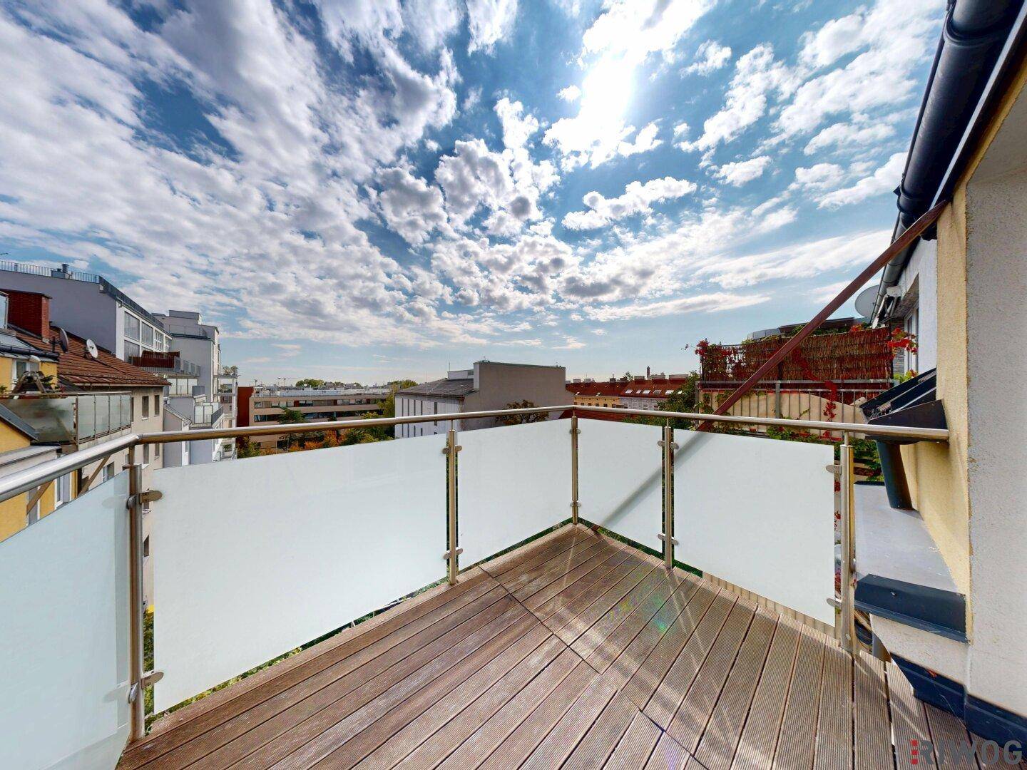 Sonniger Balkon mit Holzbelag und Glasgeländer, ideal für entspannte Stunden im Freien.